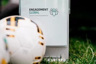 Ein Fußball liegt auf einer Wiese. Dahinter ist das Logo von Engagement Global zu sehen.