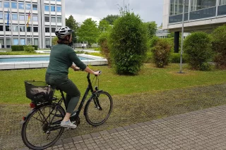 Zu sehen ist eine Frau auf einem Fahrrad in Bonn. Im Hintergrund ist das Gebäude der Bundesnetzagentur zu sehen. Foto: Engagement Global