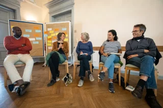 Fünf Personen sitzen in einem Stuhlkreis und unterhalten sich.