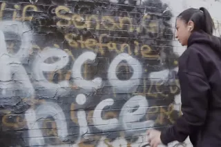 Eine Schülerin sprayt die Worte „Reconice" an eine Backsteinwand.