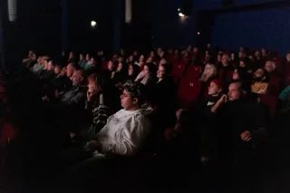 Eine Gruppe von Menschen sitzt in einem dunklen Kino und schaut auf die Leinwand.