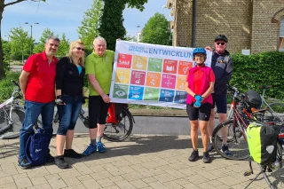 Fünf Personen in Fahrradkleidung halten ein Banner zu den Nachhaltigkeitszielen hoch.