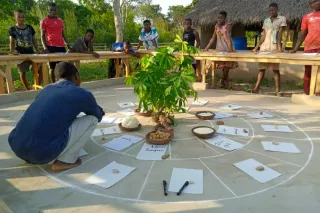Kinder stehen um einen Kreis herum, in dem eine Pflanze und verschiedene Zettel mit Informationen angeordnet sind.