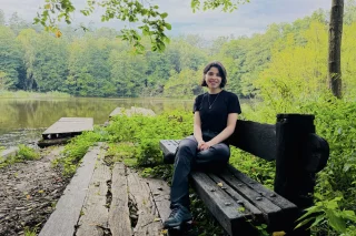 Die Freiwillige Monica Jazmin Cristaldo Jimenez sitzt auf einer Bank im Naturpark und schaut in die Kamera. Hinter ihr sind ein See und ein Wald zu sehen.