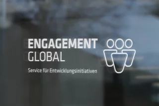 Das Logo von Engagement Global zeigt den Namen der Organisation in grauer und blauer Schrift. Zudem sind auf der rechten Seite drei Kegel zu erkennen.