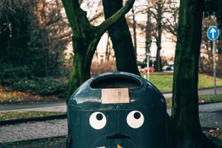 Mülleimer mit aufgeklebten Augen in einem Stadtpark.