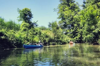 Zwei Personen in zwei Kanus auf einem Fluss.