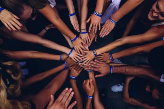 Viele Personen stehen in einem Kreis und strecken ihre Hände in die Mitte.