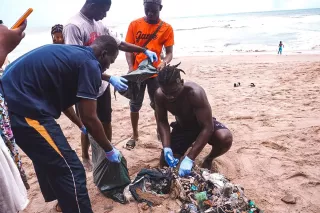 Vier Personen befinden sich an einem Strand und sortieren Plastikmüll.