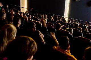 Personen sitzen in einem dunklen Kino und schauen Richtung Kinoleinwand.