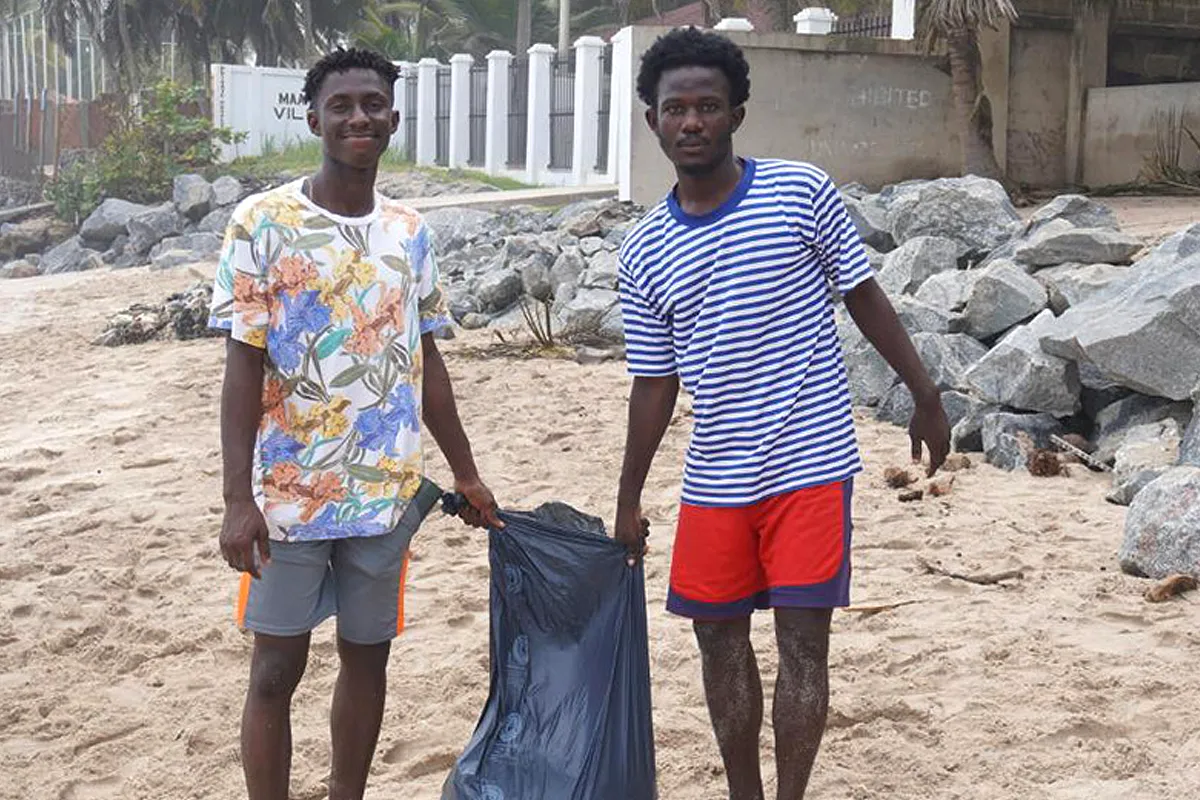 Zwei Personen stehen an einem Strand und halten gemeinsam einen halbvollen Müllbeutel.